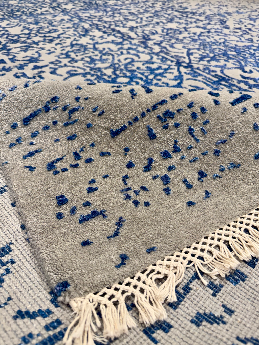Gray and blue patterned rug with tassels on a matching background